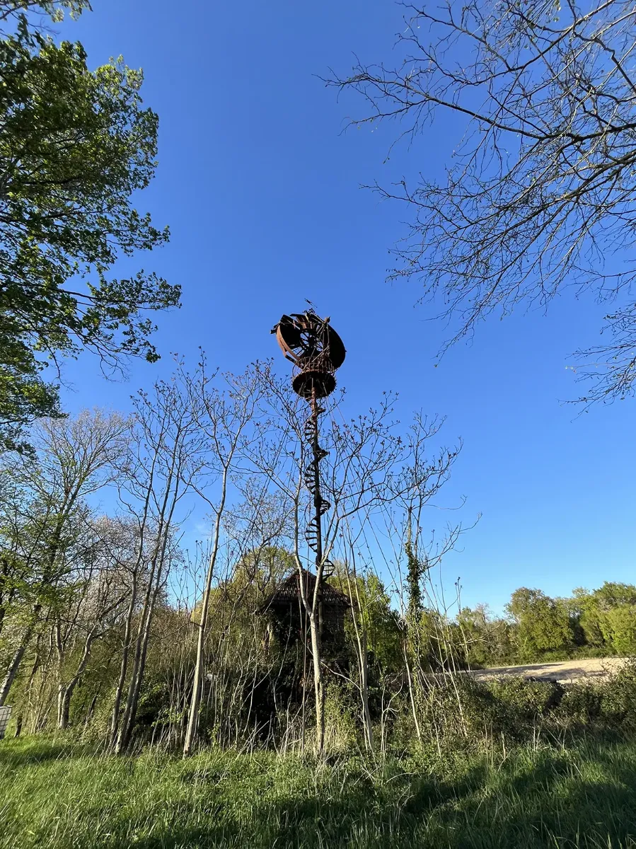 Escalier hélicoïdal en acier montant vers une plateforme perchée au-dessus des arbres, contre un ciel bleu
