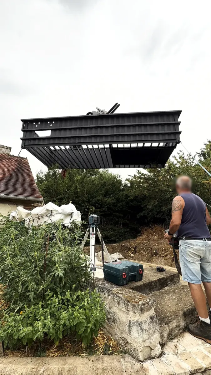 Grande structure d'acier levée à la grue au-dessus d'un jardin, compagnon suivant la manœuvre au niveau laser