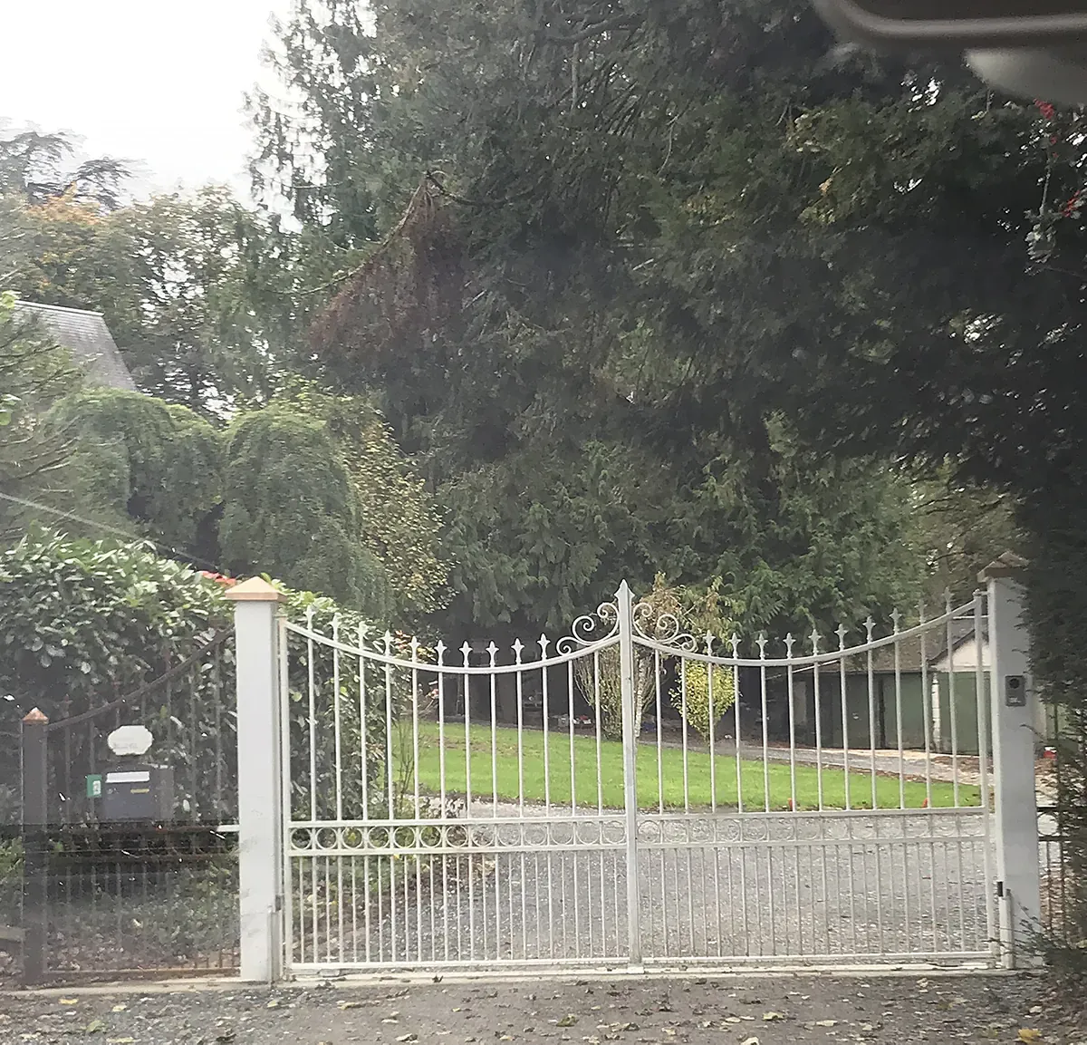 Portail en fer forgé peint en blanc, à volutes et barreaux, fermant l'allée d'une propriété