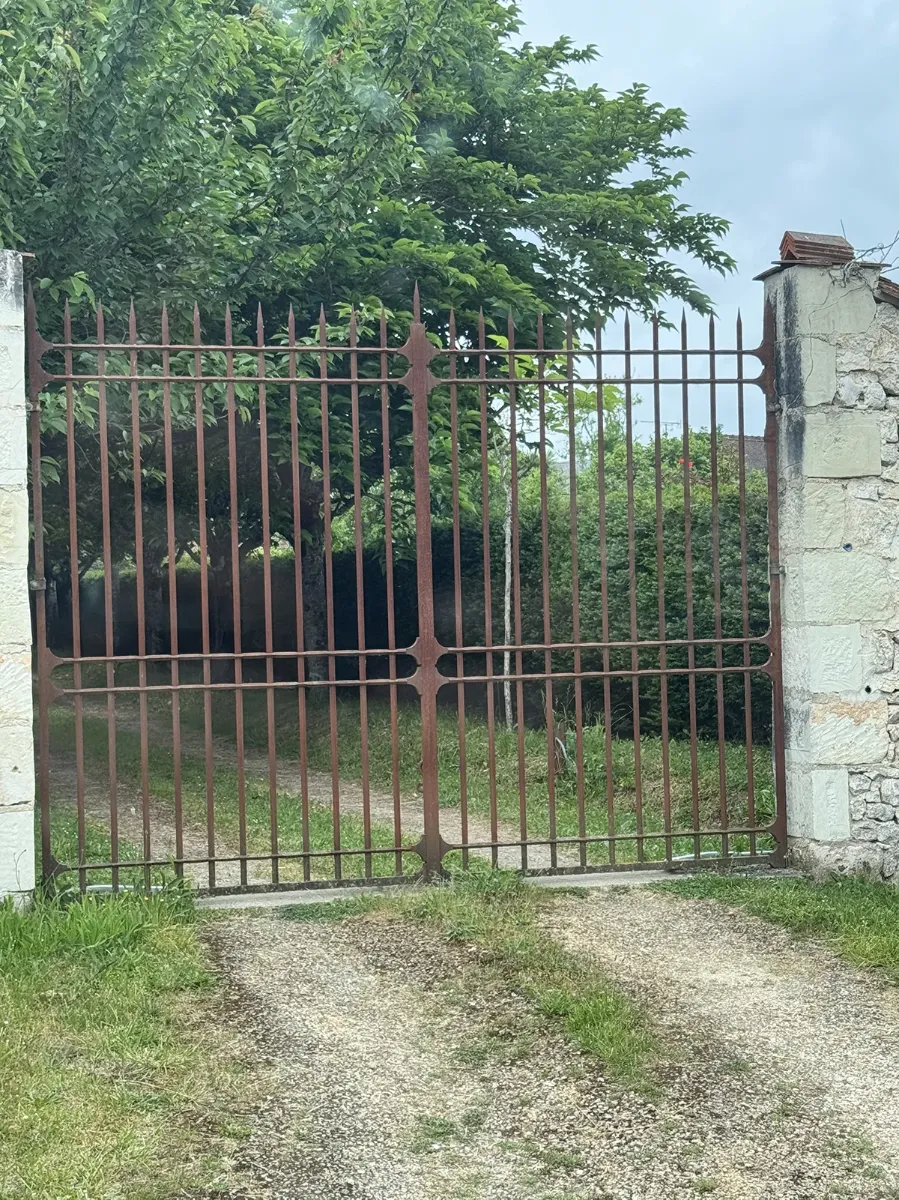 Portail ancien en fer forgé à barreaux et pointes, dressé entre deux piliers de pierre