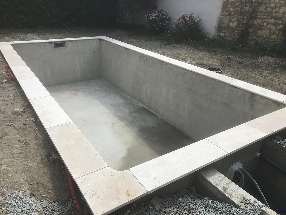 Bassin de piscine en béton lissé, ceinturé de margelles en pierre de taille, avant mise en eau