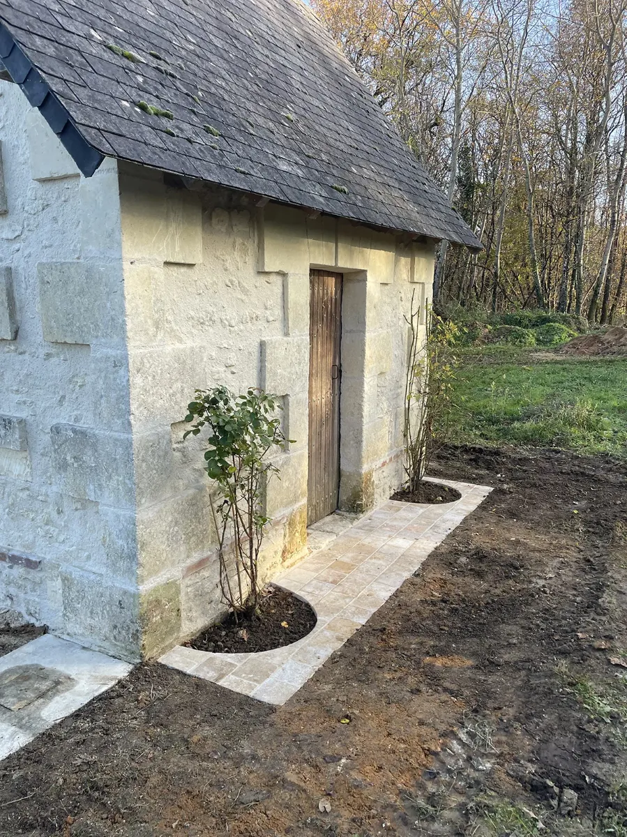 Cheminement en dalles de pierre courant au pied d'une maisonnette restaurée, réservations plantées