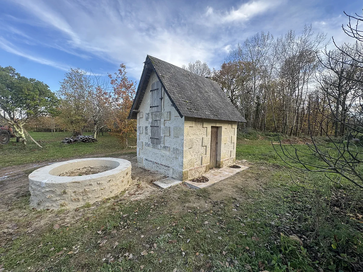Vasque de pierre et maisonnette de verger restaurée, sous un ciel de traîne