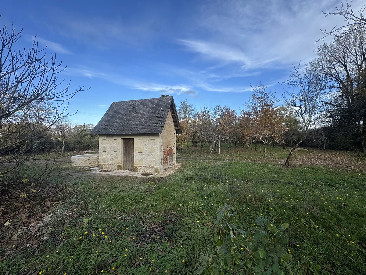 Maisonnette de pierre restaurée et sa vasque, au milieu d'un verger, sous un grand ciel d'hiver