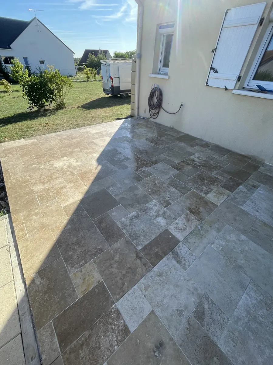 Terrasse en dalles de travertin posées en opus le long d'une maison, fraîchement lavée