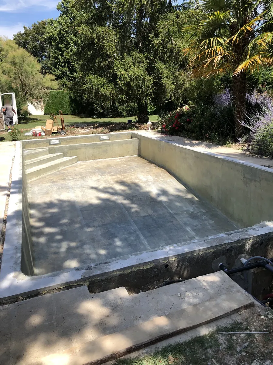Bassin de piscine en béton brut avec son escalier, avant enduit, dans un jardin planté