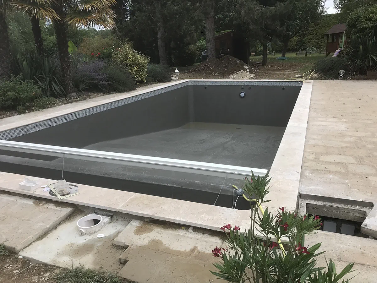 Bassin de piscine gris avec sa banquette et son volet immergé, margelles de travertin en place