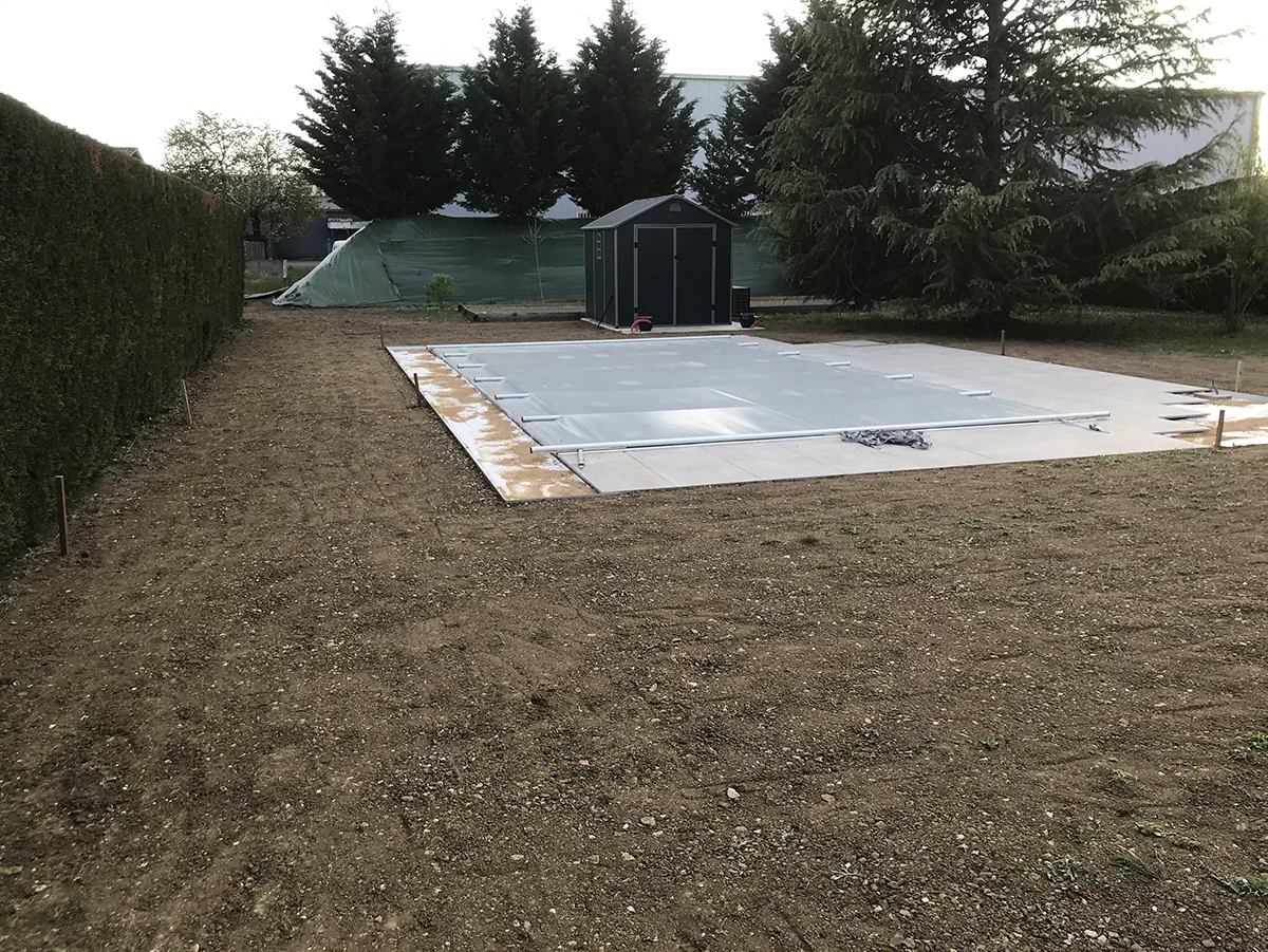 Dalle de béton coulée et bâchée au milieu d'un terrain nu, abri de jardin à l'arrière