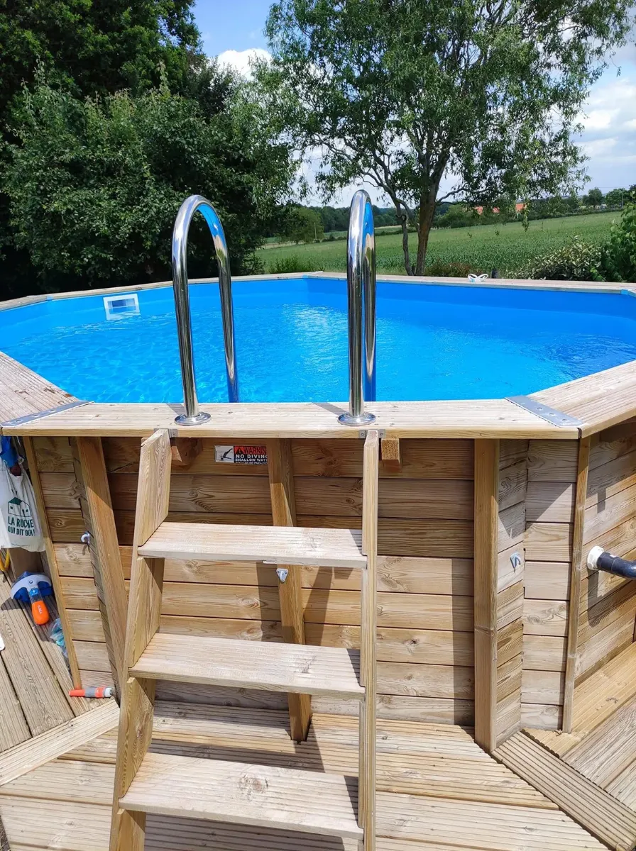 Échelle de bois et margelle d'une piscine hors-sol octogonale, ouverte sur les champs