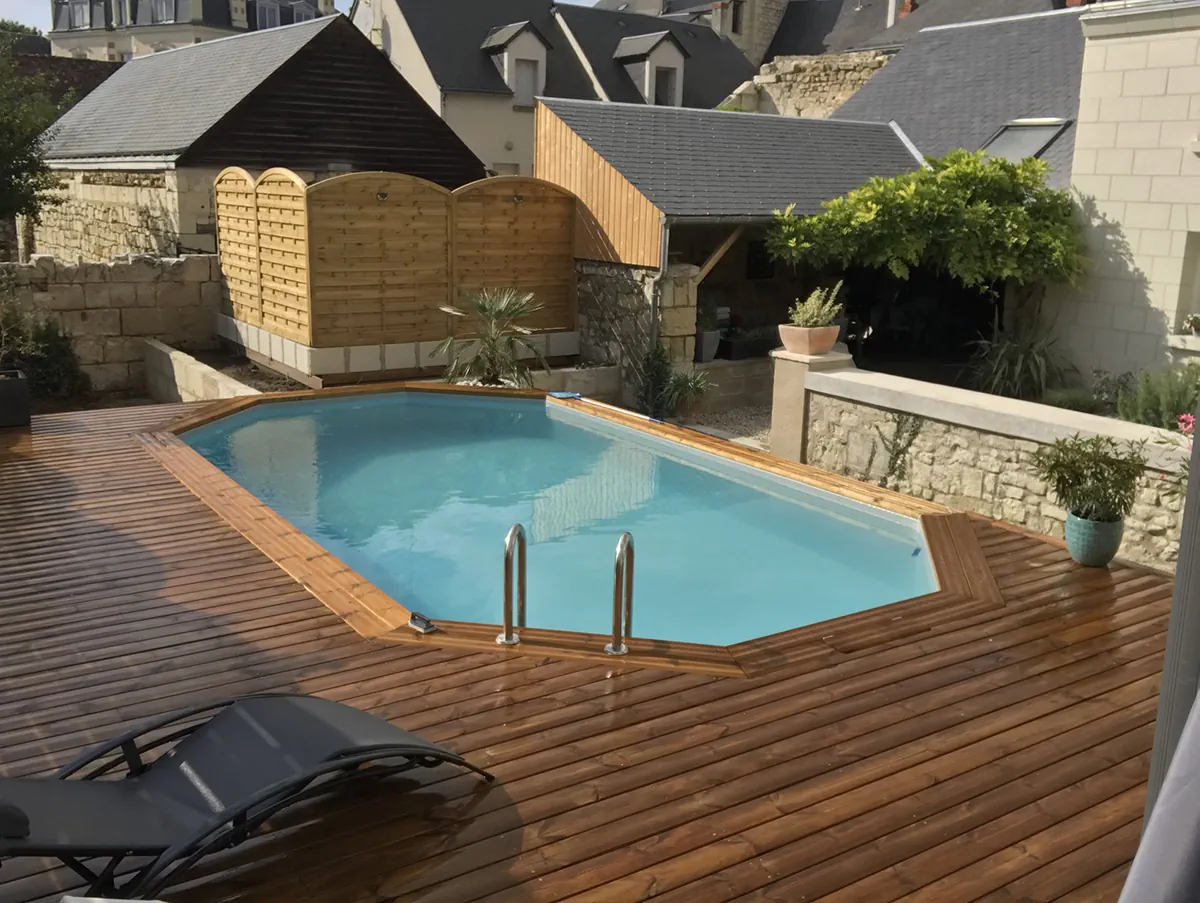 Piscine bois octogonale et sa large terrasse en lames, dans un jardin de ville cerné de toits d'ardoise