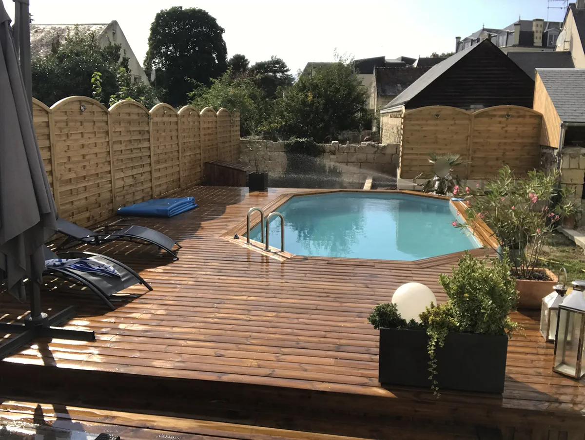 Piscine bois et sa terrasse fraîchement lavée, fermée par des palissades à l'arase cintrée