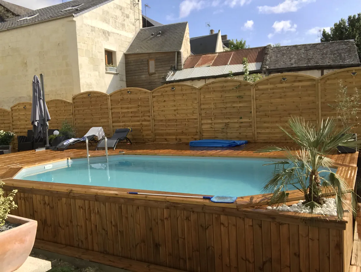 Piscine bois octogonale, terrasse en lames et palmier en pot, devant des murs de tuffeau