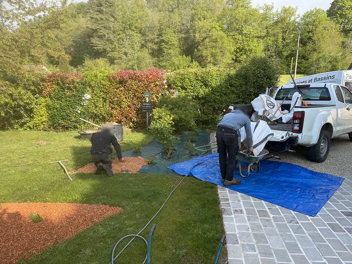 Deux compagnons étalant un paillage de gravier orangé sur toile, pick-up Pausity chargé de big-bags