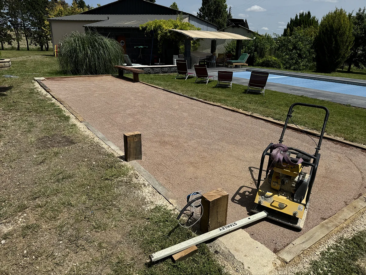 Plaque vibrante posée sur un terrain de boules en cours de finition, piscine et terrasse en arrière-plan