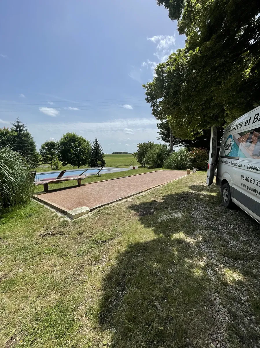 Terrain de boules achevé au bord d'une piscine, fourgon Pausity Piscines et Bassins garé sur la droite