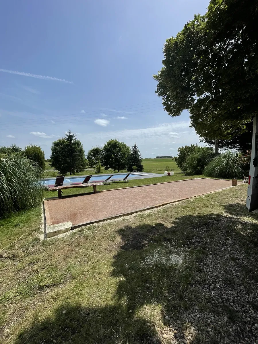 Terrain de boules terminé le long d'une piscine, ouvert sur la campagne, en plein soleil d'été