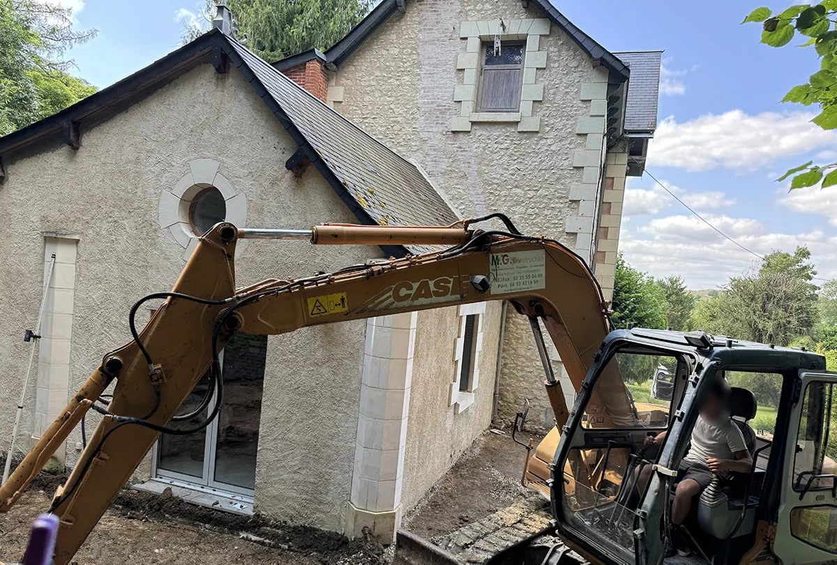 Pelle mécanique dérasant le sol au pied d'une maison de pierre en rénovation
