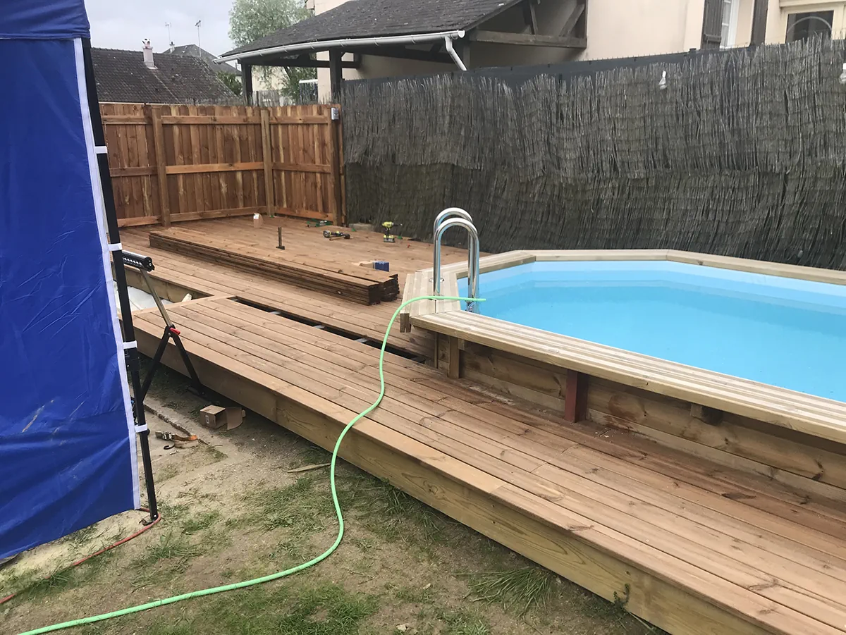 Lames de terrasse posées le long d'une piscine hors-sol en bois, chantier en cours de finition