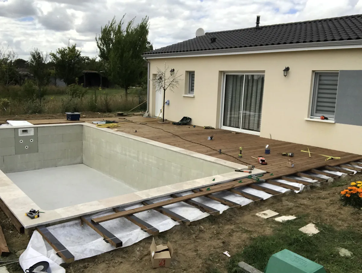 Lames de bois en cours de pose sur lambourdes le long d'un bassin de piscine maçonné, outillage étalé