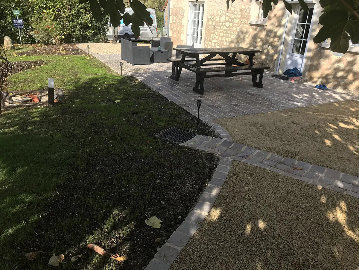 Terrasse pavée prolongée de cheminements bordés de pavés, entre pelouse et allée de gravier