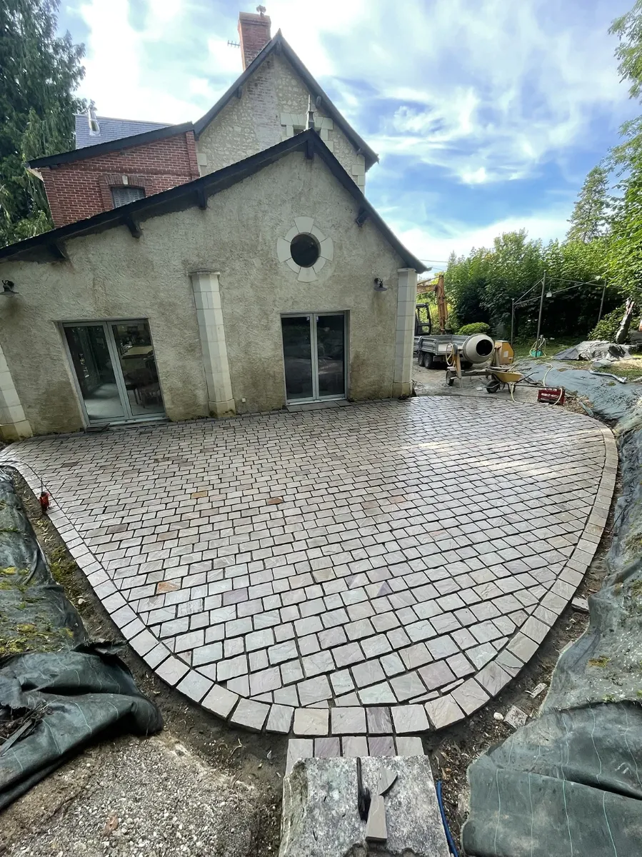 Terrasse en pavés de pierre au tracé en demi-cercle, achevée devant le pignon d'une maison ancienne