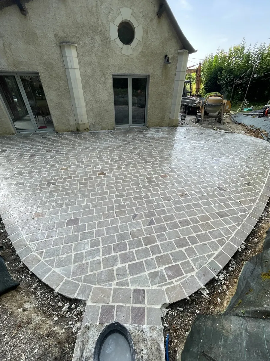 Terrasse en pavés de pierre au tracé courbe, vue en plongée, bétonnière encore sur le chantier