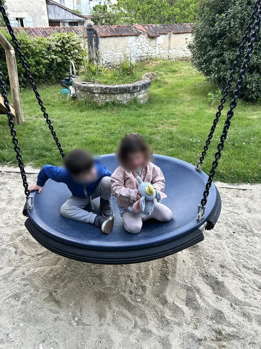 Balançoire nid suspendue à ses chaînes au-dessus d'une aire de sable, deux enfants assis dessus
