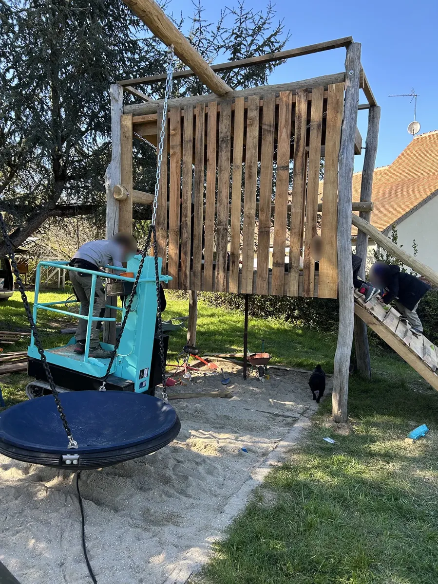 Compagnons montant la palissade d'une cabane de jeux depuis une nacelle, balançoire nid déjà suspendue