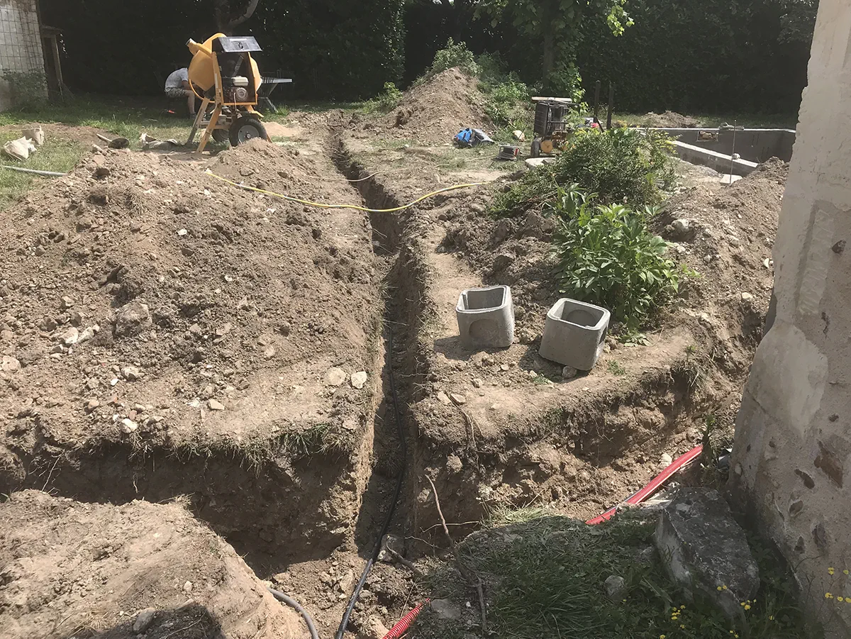 Tranchées de réseaux ouvertes en croix dans un jardin, regards en béton posés en attente de raccordement
